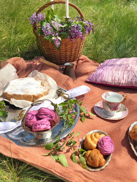 Picnic with assorted pastries and romantic lilac flowers in basket placed on green lawn
